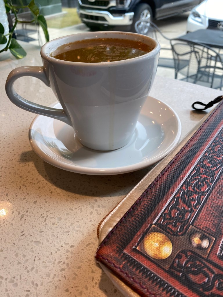 Large mug of hot apple cide on a coffee shop table next to the corner of a decorative laptop case