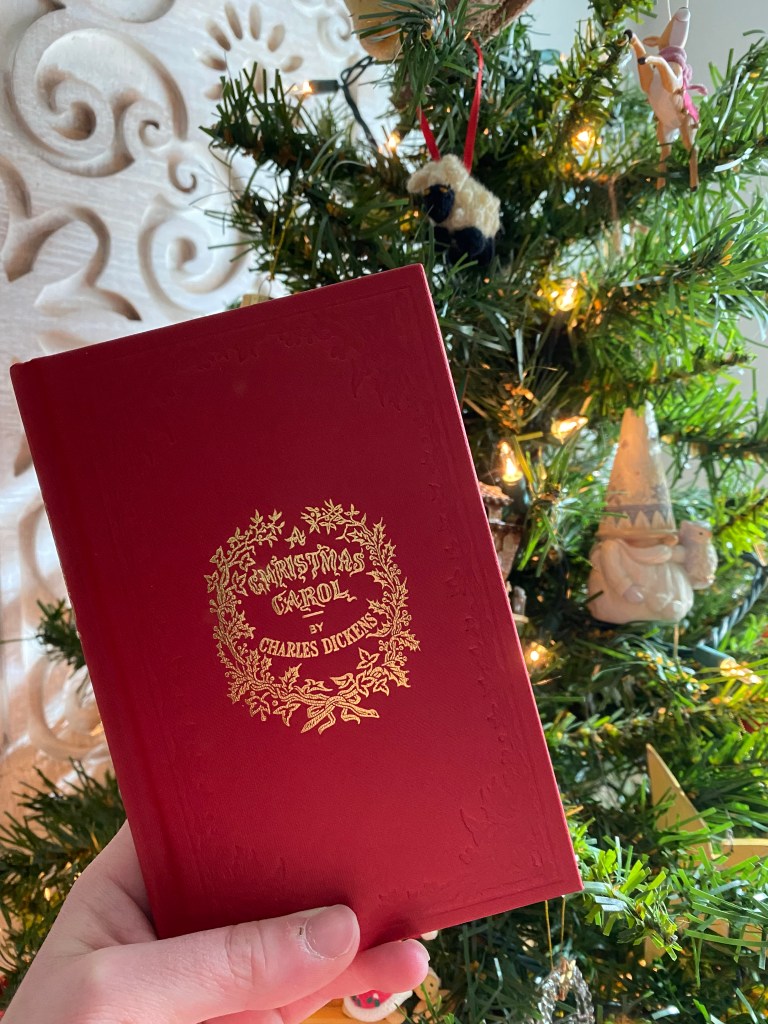 A recreation of the original printing of A Christmas Carol Book in front of a Christmas Tree