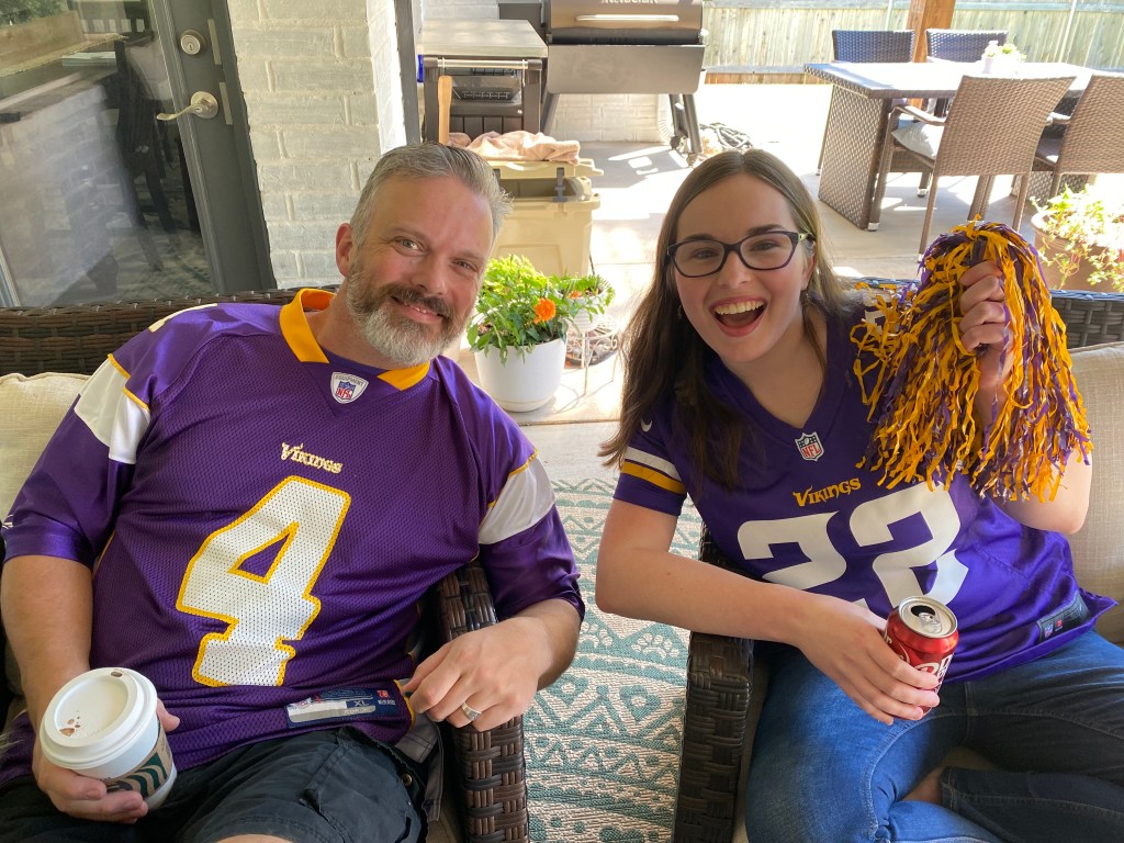 Dad and daughter in Minnesota Vikings jerseys watching football on the back porch